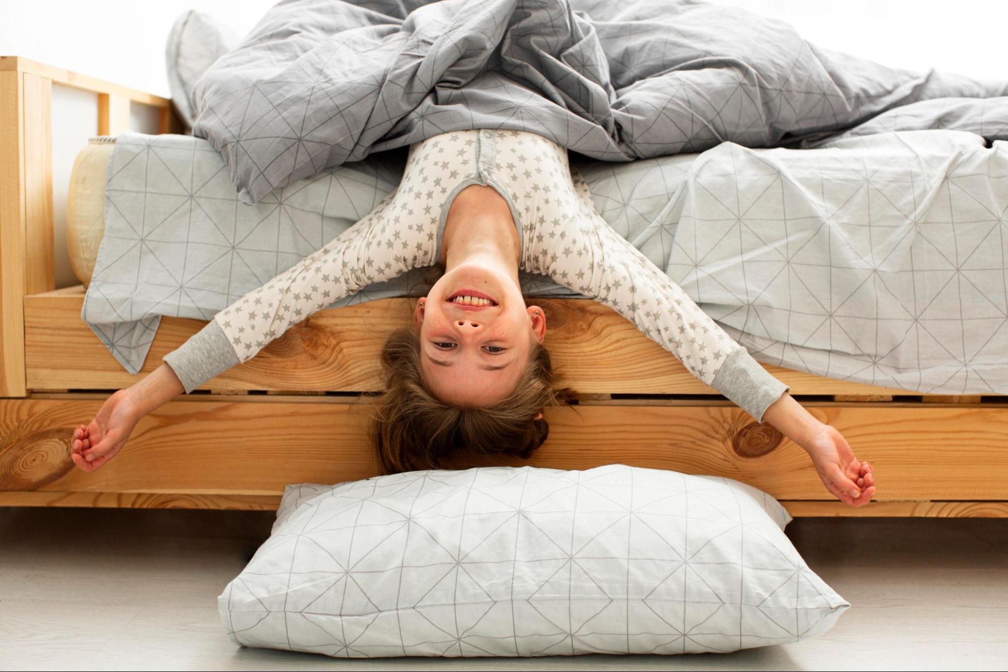 A young girl lies on her back in a cozy bed, surrounded by soft pillows and blankets, looking relaxed and content.