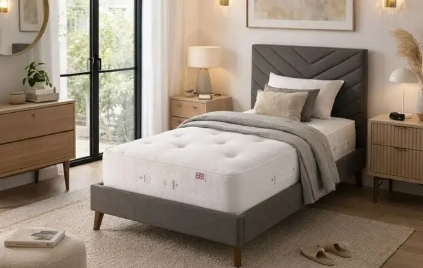 A mattress displayed on a single ottoman bed that’s upholstered in a grey material.